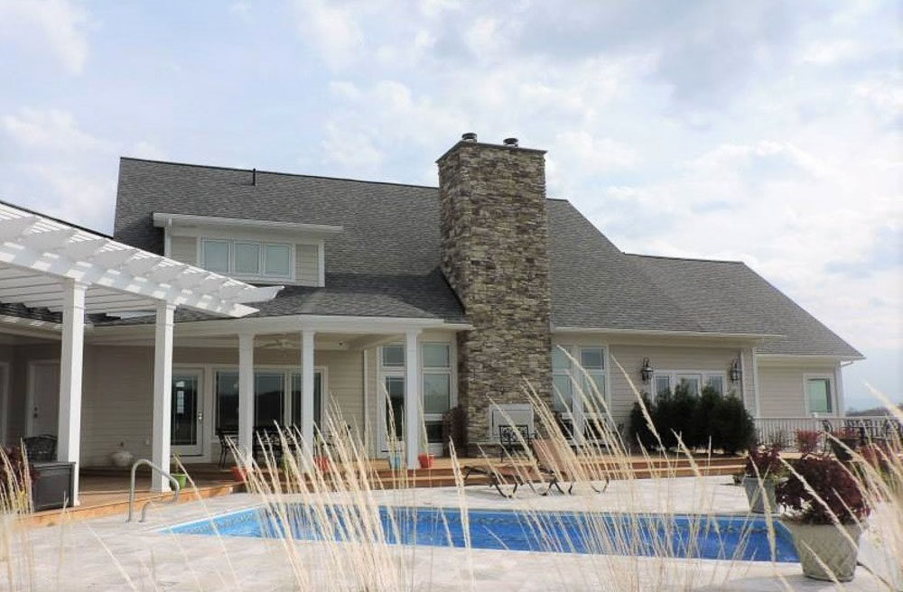 Rear of a stone and shingle residence with a pergola and pool